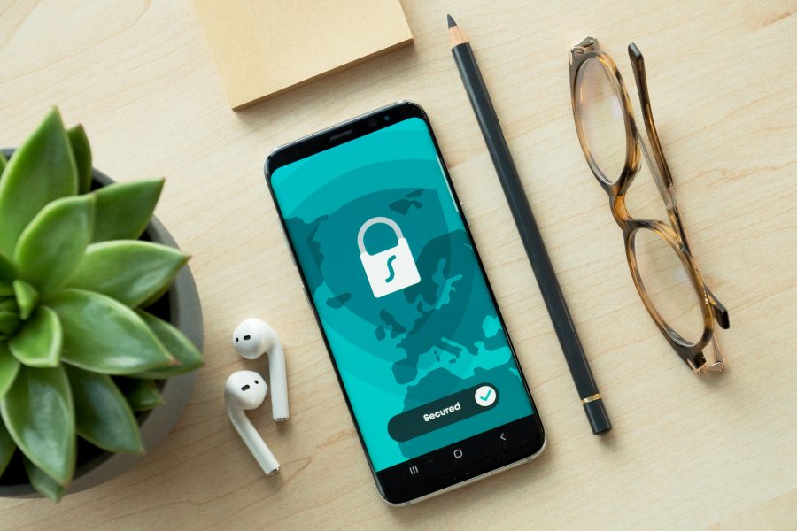 Black smartphone with secure mobile app running next to a pencil, glasses, headphones and a cactus