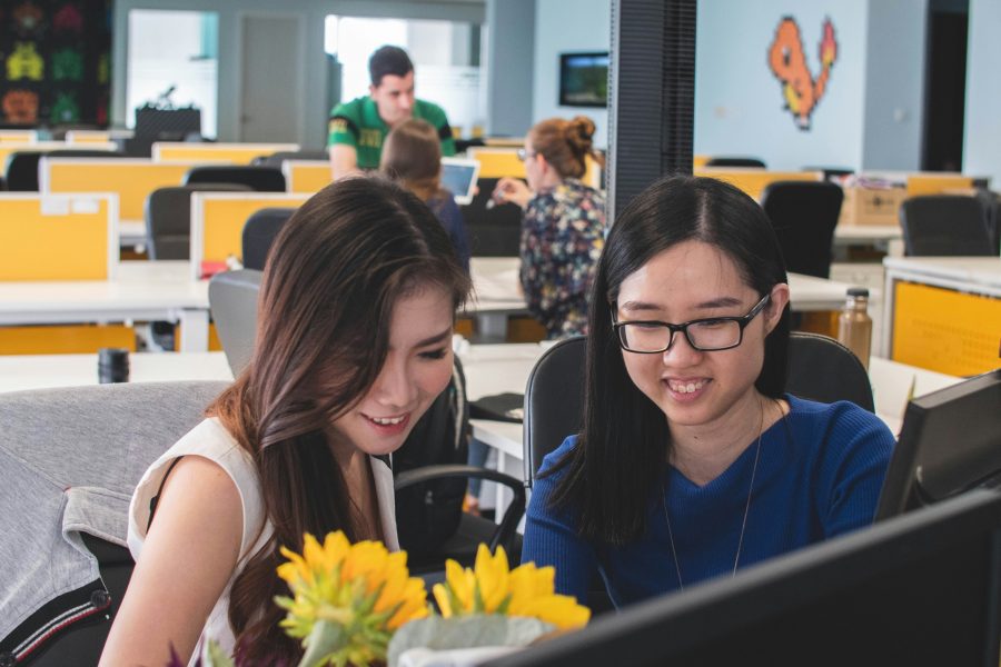 Two female developers smiling at a screen in an open-concept office while using hot reloading to test their app