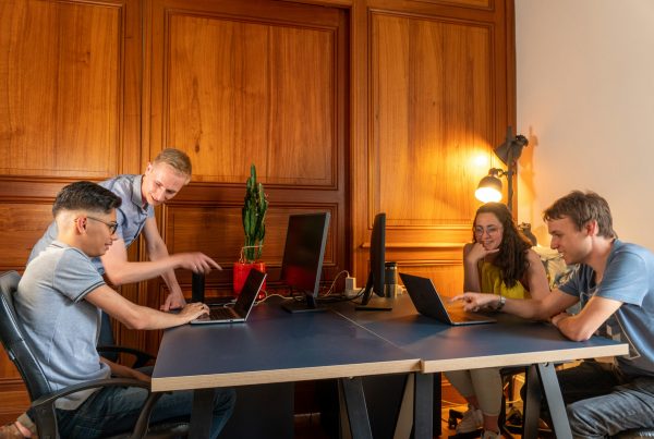 Four students are working on laptops in a wood-paneled room