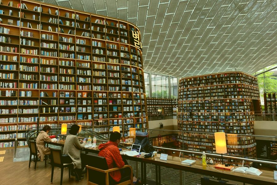 A modern library using a relational database to stay organized, with bookshelves that reach the ceiling. At the bottom, there are people sat at desks using their laptops.
