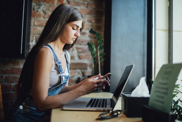Woman at cafe works on her progressive web app (PWA) by using her phone and laptop
